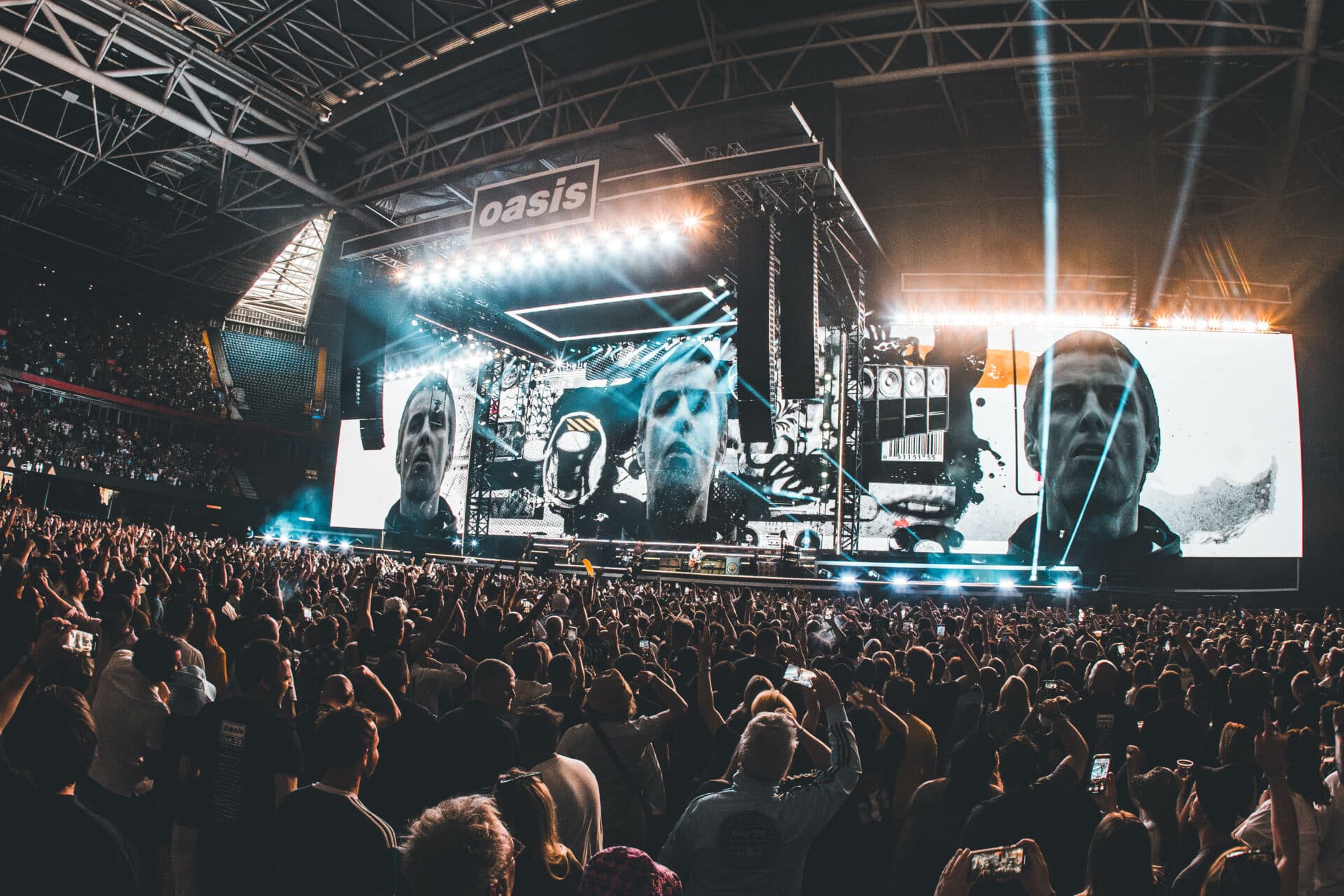 Crowd at an Oasis Live '25 stadium concert, hands raised under the stage lights